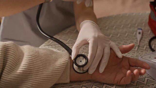 Close up of young paramedic adjusting mask and checking pulse of senior patient while they sitting at dining table