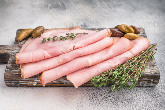 Italian cured pork slices with thyme and olives on a rustic wooden board against a textured gray background with ample copy space.