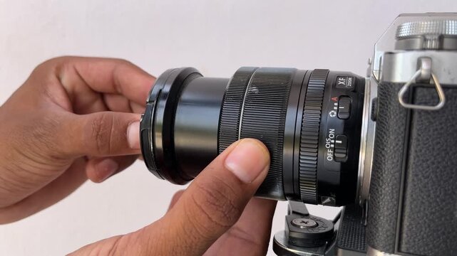 Close-up of a hand attaching a protective lens cap to a mirrorless camera lens