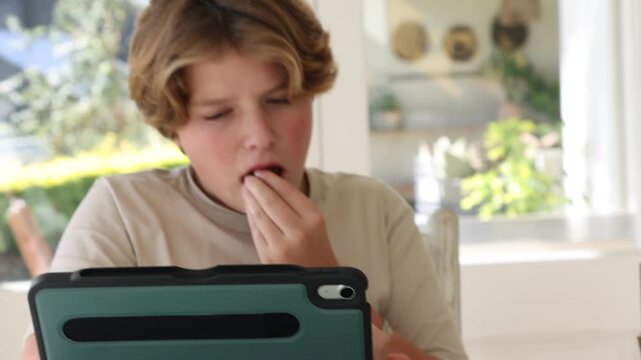 12 year old boy eating box lunch in kitchen using tablet computer