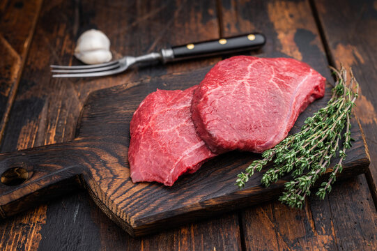Marbled Wagyu beef chuck resembling angus and yakiniku cuts arranged with thyme and garlic on dark wood background great for food photography.