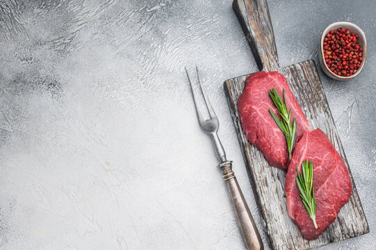 Fresh raw Wagyu chuck steak resembling zabuton or Denver cut arranged with herbs on weathered wood against bright gray backdrop ideal for premium food photography.