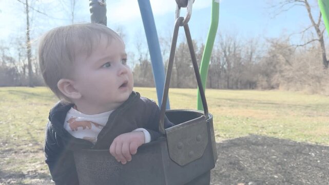 Young boy hanging in child swing at playground 4k
