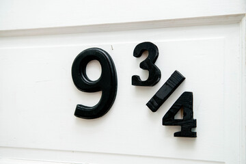 Naklejka premium Close-up of a white front door to a bookstore or house with the numbers 9 3/4 posted in large black numerals. The building's street address calls to mind the hidden train station entrance Harry Potter