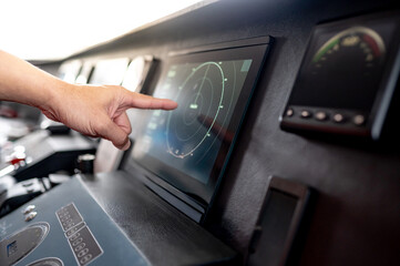 Captain hand pointing at marine radar monitor screen or GPS navigation map on boat dashboard. Nautical vessel control system in wheelhouse or ship bridge. Modern boating technology and operation © zephyr_p
