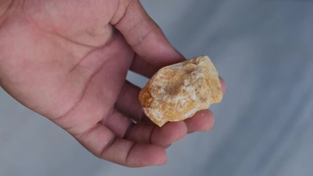 Close-up of a hand holding a piece of raw jaggery