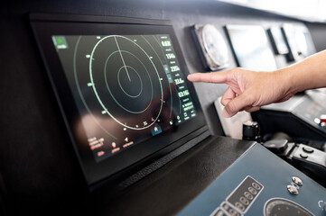Captain hand pointing at marine radar monitor screen or GPS navigation map on boat dashboard. Nautical vessel control system in wheelhouse or ship bridge. Modern boating technology and operation © zephyr_p