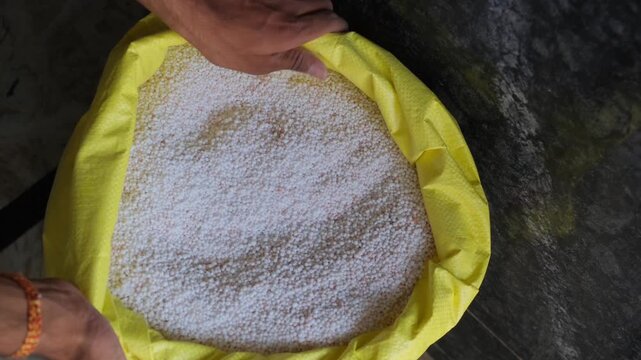 Hands folding the edges of a yellow bag containing granular urea fertilizer