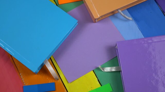 Multicolored notepads and stickers paper lie on a wooden rainbow colors board, top view  