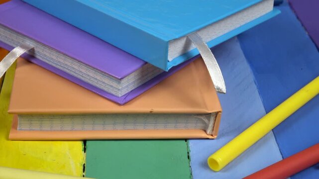 Multicolored notepads and ballpoint pens lie on a wooden rainbow colors board, side view  
