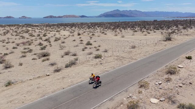 A mature man and woman bike together near La Gringa by the Bahia De Los Angeles, showing the desert landscape and sea.