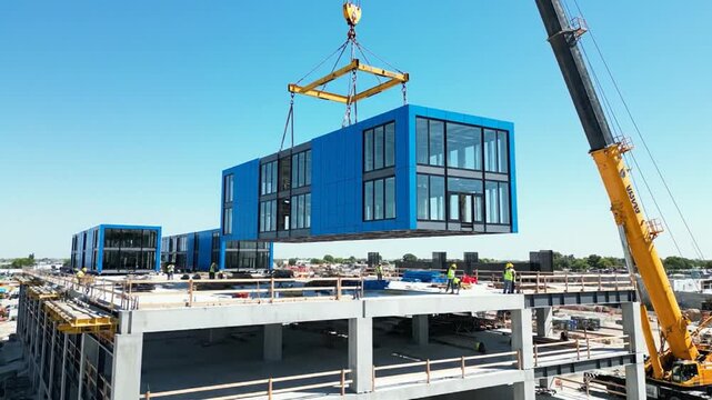 Massive crane lifts prefabricated blue modular building sections into place on construction site