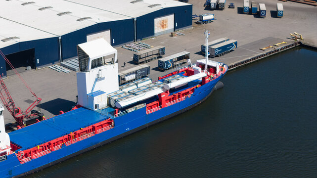 Aerial view of a cargo ship docked at the Westpoort industrial harbor with warehouses and logistics trucks in Amsterdam, North Holland, Netherlands.