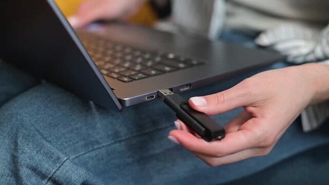 A close-up of a person trying to insert a USB drive into a laptop while sitting at the computer. The flash drive won't insert