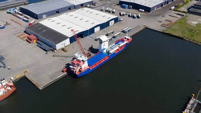 Aerial view of the Westpoort industrial area with a cargo ship docked at the pier next to warehouses and trucks in Amsterdam, North Holland, Netherlands.