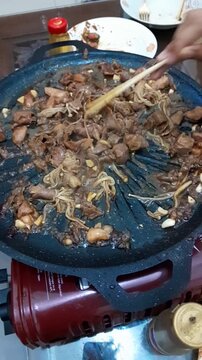 Close up of cooking delicious sliced beef, enoki mushrooms, and garlic on a hot grill plate pan. Top view of preparing Asian barbecue or stir fry.