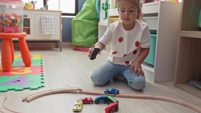Girl reaches hand to toy car on wooden train track while kneeling in a building playroom; imagination concentration.