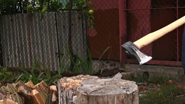 Axe hitting log, splitting wood in backyard. Person in red hoodie swinging axe, pieces of wood breaking apart, natural environment, active lifestyle, outdoor concept, detail shot.