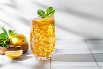 Fototapeta premium Iced tea with lemon and mint in a glass on a light tile background with shadows