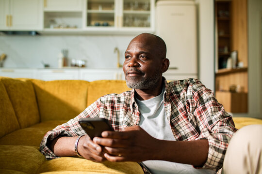 Mature man relaxing on sofa at home with smartphone