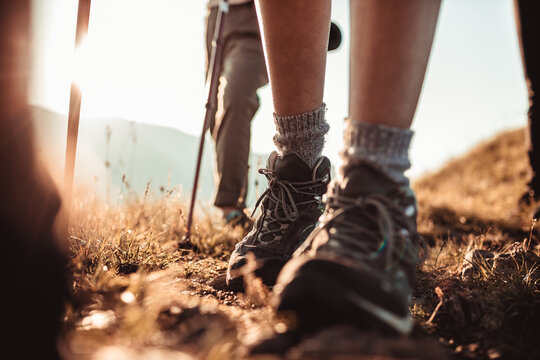 Hikers walking with trekking poles on mountain trail at sunrise
