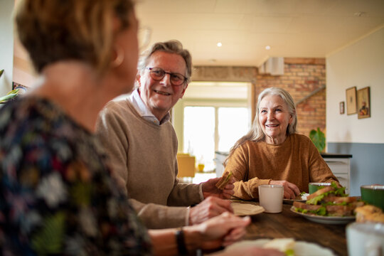 Smiling senior friends sharing lunch at home kitchen