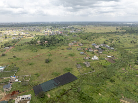 Aerial view of scattered residential houses and green fields under a cloudy sky in a developing suburban area in Thika, Kiambu County, Kenya.