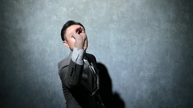 グレー背景でダーツを投げるスーツを着た日本人男性