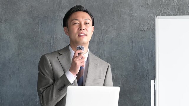 グレー背景でプレゼンをするスーツを着た日本人男性