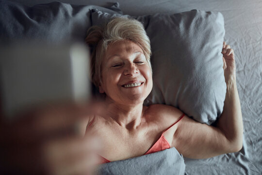 Smiling senior woman taking selfie in bed at home