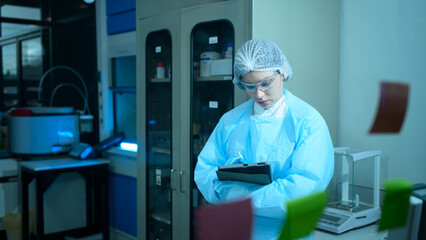 Naklejka premium Female Lab Technician in Protective Gear Using Tablet in Modern Scientific Laboratory