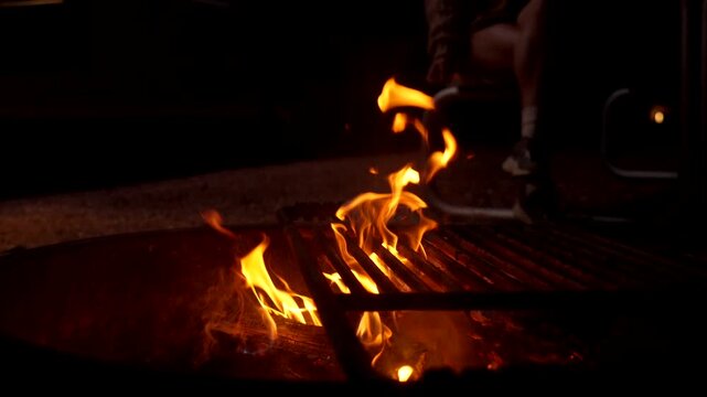 Vibrant bonfire flames burning brightly in a metal fire pit at a campsite during a dark evening, providing warmth and a cozy atmosphere for outdoor recreational activities