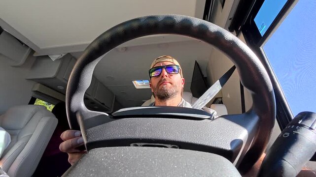 Focused man wearing sunglasses and a cap driving a motorhome during a sunny day, experiencing the freedom of van life on a scenic road trip through the united states of america