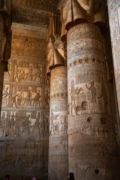 Epic Dendera Hathor temple ancient interior vertical panorama. 
Cinematic low angle view of historic hypostyle hall, 
giant columns with goddess capitals and carved hieroglyph bas-relief walls.
