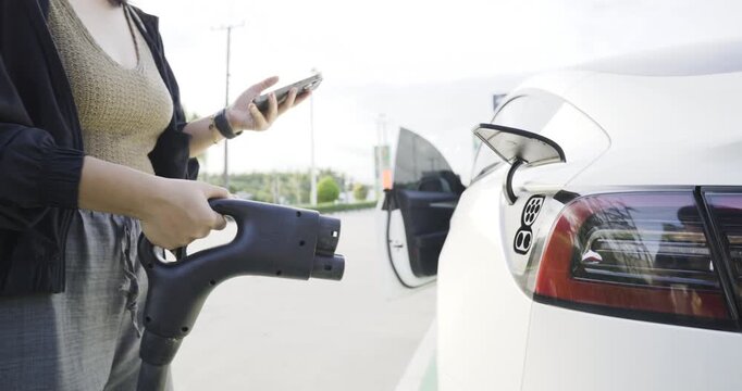 Casual woman use outdoor station EV car charge with mobile phone transport technology