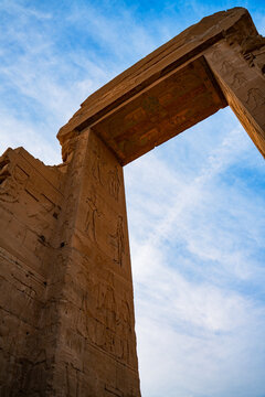 Epic Dendera temple ruins ancient Egyptian architecture vertical panorama. 
Cinematic low angle view of historic Domitian gateway propylon, 
carved pharaoh hieroglyphs bas relief and blue sky.
