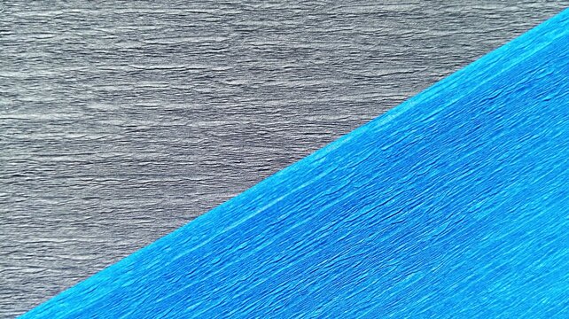 Textured corrugated paper backdrop featuring a contrast of graphite gray and vibrant cobalt blue colors. Two-tone crepe paper texture background with diagonal split in charcoal grey and bright blue