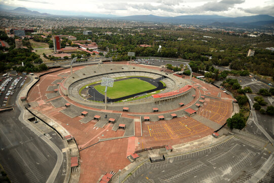 Aerial view of Estadio Olimpico Universitario showing the green pitch and concrete stands surrounded by parking lots and trees in Ciudad de Mexico, Ciudad de Mexico, Mexico.