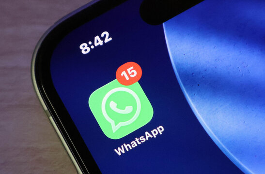 Closeup of a smartphone screen showing the whatsapp application icon with a notification badge indicating 15 unread messages
