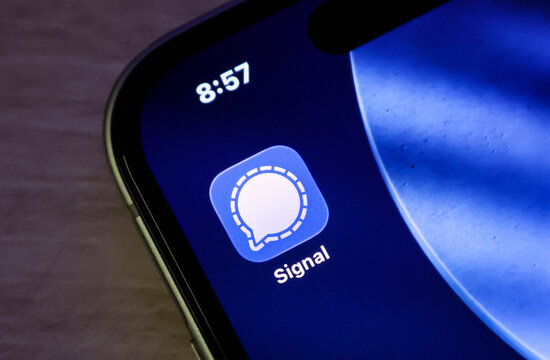 Closeup of the signal messaging app icon on a smartphone screen, displaying the iconic white speech bubble logo against a blue background