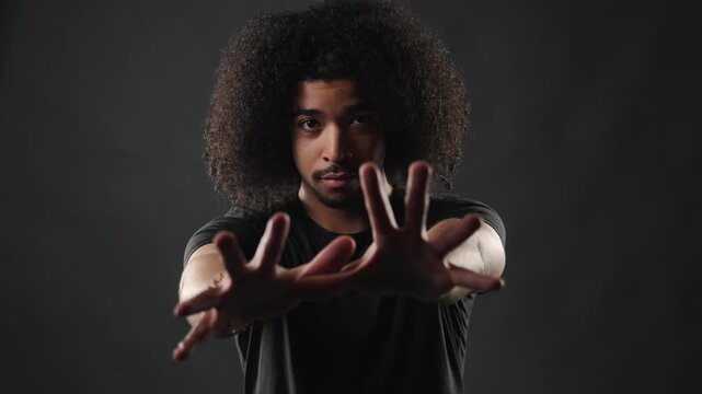 A stop gesture and boundary setting concept. A young man with afro hair extends his hands forward, conveying a sense of pushing away or creating distance.