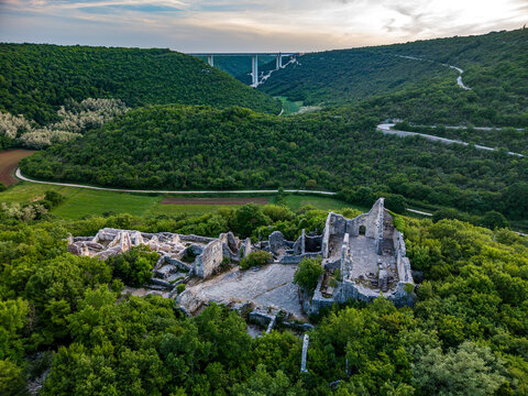 Aerial view of the medieval Dvigrad ruins surrounded by lush green forests and the Lim valley with a high bridge in the distance in Kanfanar, Istria County, Croatia.