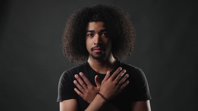 A confident young man with a voluminous afro hairstyle and a dark t shirt poses against a dramatic gray background. His serious expression and direct gaze create an impactful portrait, highlighting hi