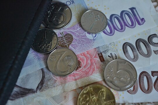 Close-up of Czech koruna banknotes and coins spilling out of a black leather wallet on a textured background.