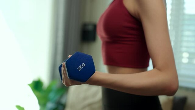 Close-up Young woman doing strength training with dumbbells and kettlebells at home. Fitness for longevity, healthy aging, muscle strength, wellness and active lifestyle concept.

