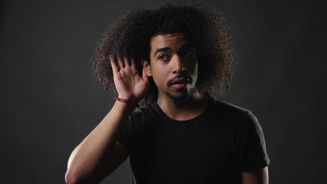 Emotional expression and self reflection are conveyed by a young man with curly hair looking down and touching his chest in a thoughtful pose. This studio portrait captures a moment of introspection, 