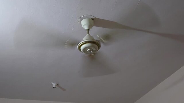 An indoor shot reveals a fast-spinning white ceiling fan struggling against the sweltering heat. The continuous movement emphasizes the oppressive indoor temperatures caused by extreme climate waves