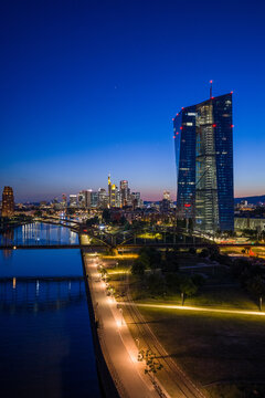 Aerial view of the illuminated ECB Tower skyscraper overlooking the Main river and the city skyline at twilight in Frankfurt am Main, Hessen, Germany.