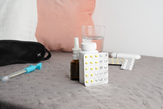 Still life of medication, sleep mask and water for travel sickness or insomnia. Remedies for jet lag on a bed. Soft lighting, neutral colors of pink, grey and white. Healthcare and travel concept