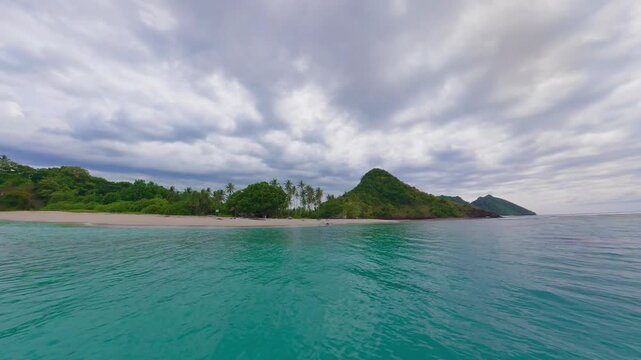 Point of View from Speedboat Arriving at Masare Island with Pristine White Sand Beach and Lush Green Hills under a Dramatic Sky in North Sulawesi Indonesia